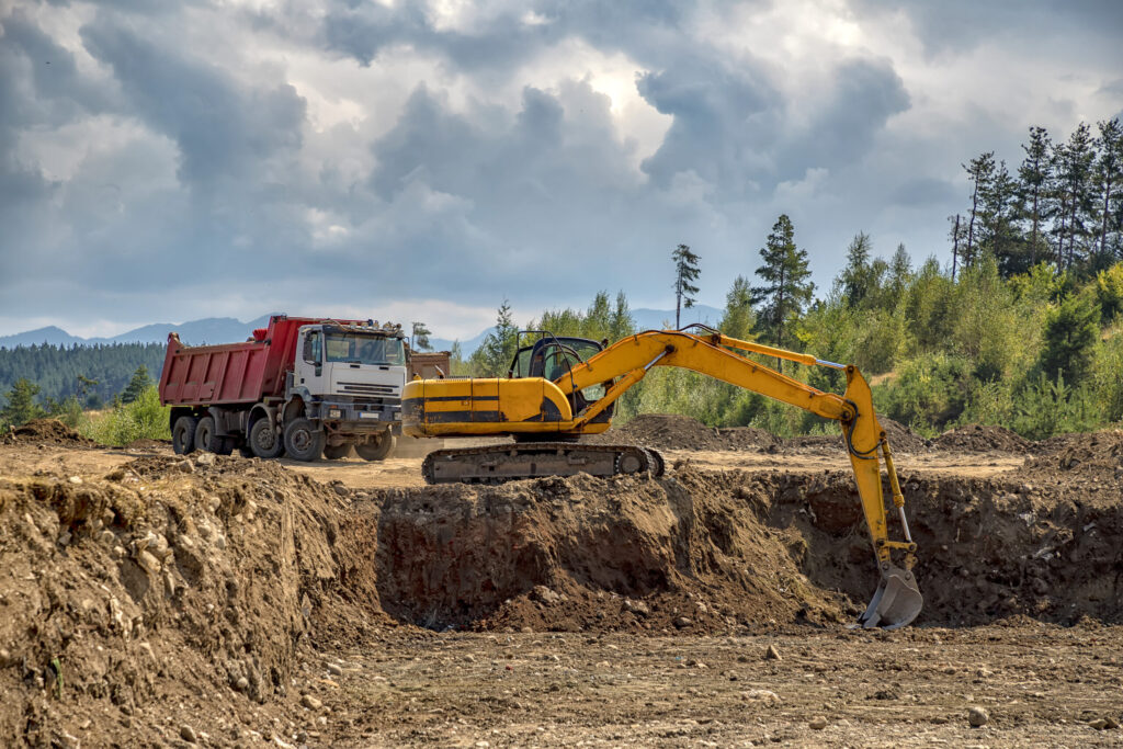 Yellow excavator and empty truck working at the construction site